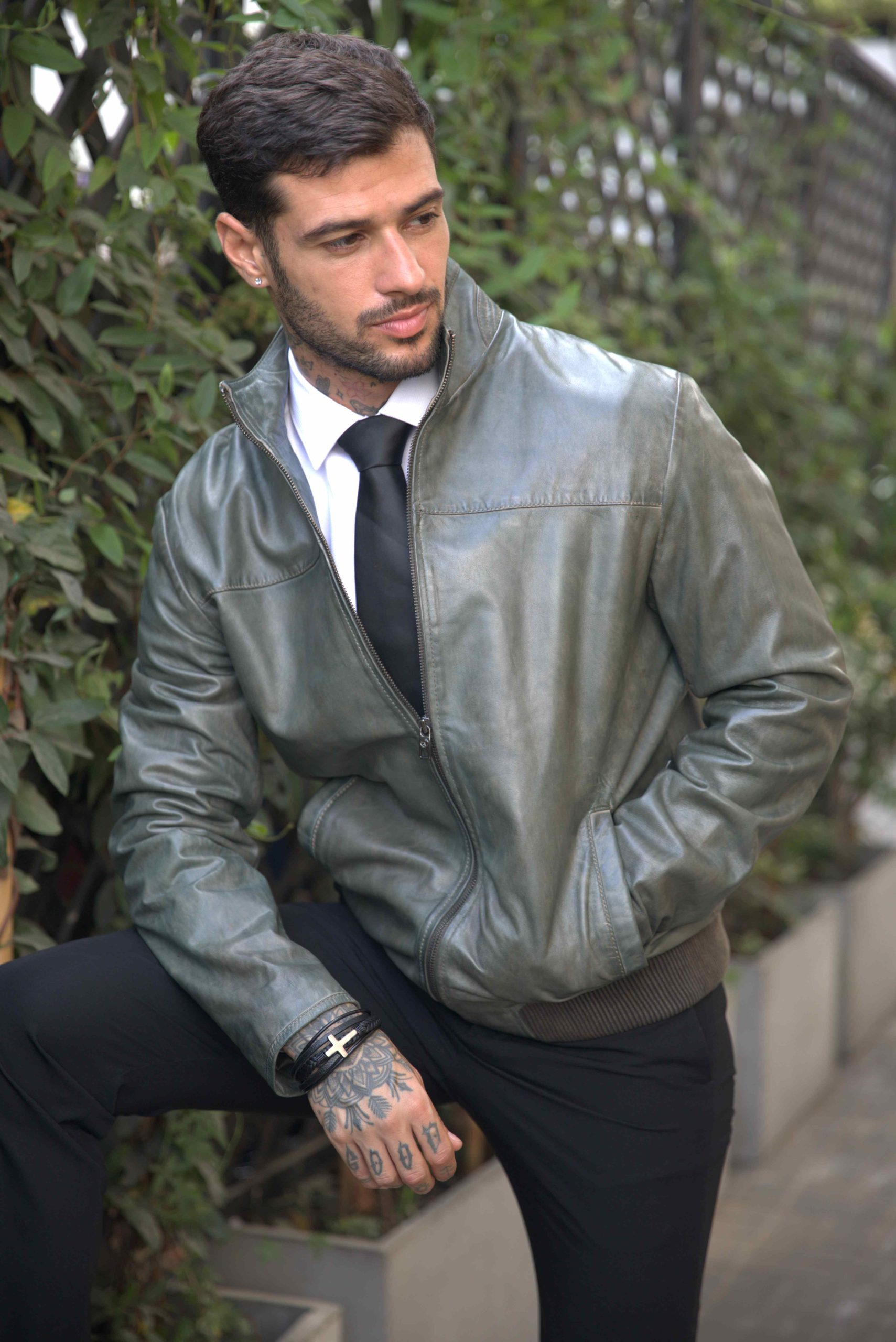 casaca de cuero Renzo Costa en tono verde olivo, combinada con camisa blanca, corbata negra y pantalón oscuro.